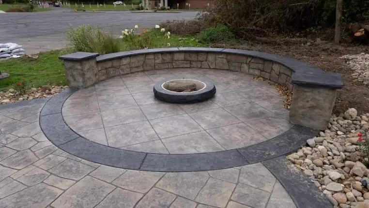 Curved stamped concrete patio with a built-in fire pit and seating wall by OTM Concrete