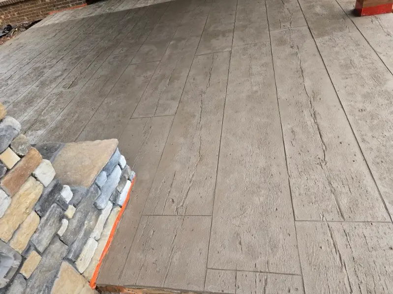 Wood plank stamped concrete patio beside a natural stone seating wall by OTM Concrete